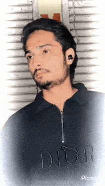 a man wearing a black dior shirt stands in front of a wall