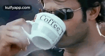 a man wearing sunglasses is drinking a cup of coffee from a mug .