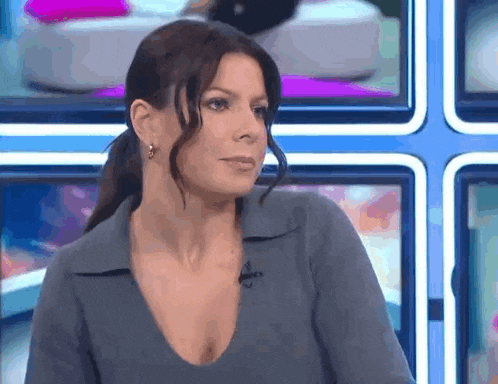a woman with a ponytail and a plunging neckline is standing in front of a television .