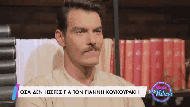 a man with a mustache is sitting in front of a stack of books and a sign that says nancy & banazhs