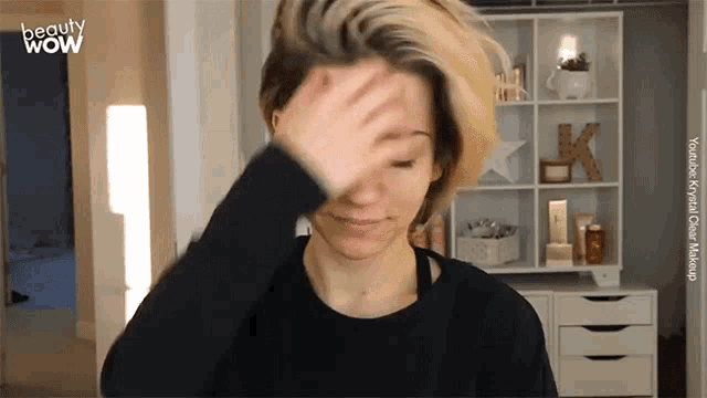 a woman adjusts her hair in front of a shelf that says k on it