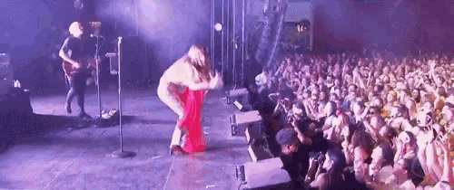 a woman in a red dress is dancing on stage in front of a crowd