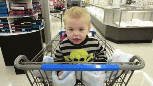 a little boy wearing a skull sweater is sitting in a shopping cart