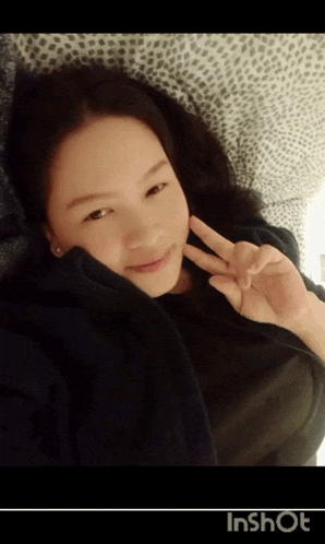 a girl is laying on a bed and making a peace sign with her hands