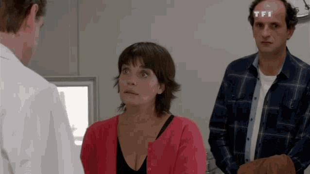 a man with a tfi logo on his forehead talks to a woman in a pink cardigan
