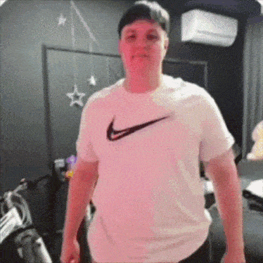 a man wearing a white nike t-shirt is standing in a bedroom .
