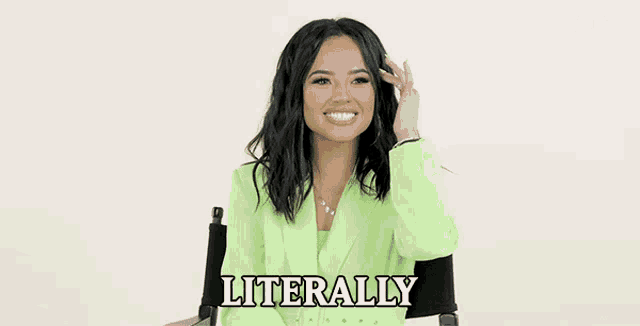 a woman in a green suit is sitting in a chair and smiling while holding her hair .