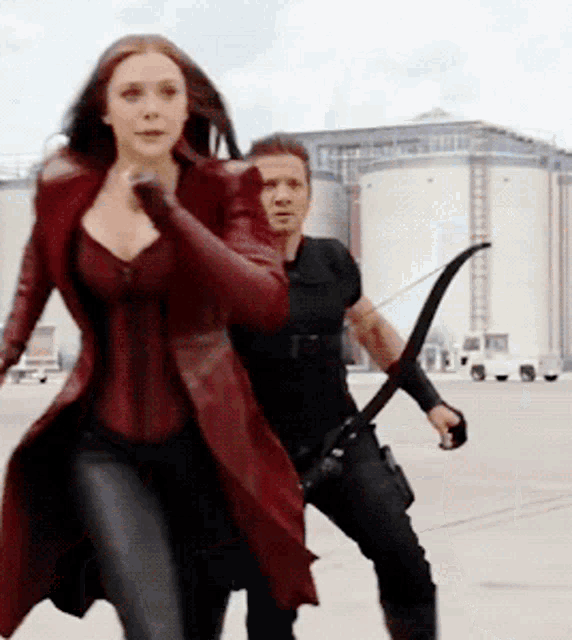 a woman in a red coat is running next to a man with a bow