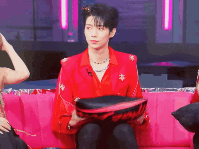 a man in a red jacket is sitting on a pink couch holding a pillow that says swag