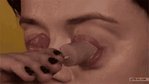 a woman is eating a popsicle with a spoon in her mouth .