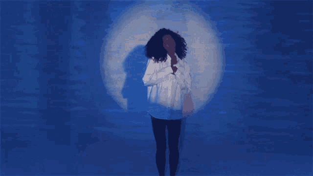 a woman in a white shirt stands in front of a blue wall