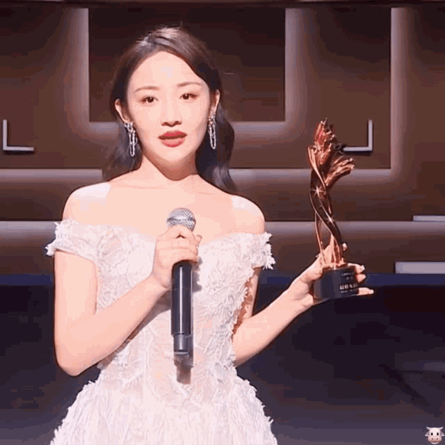 a woman in a white dress holding a microphone and a trophy