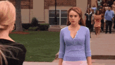a woman in a purple shirt and pink skirt is standing next to another woman on a sidewalk .