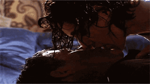 a man and a woman kissing on a bed with blue sheets