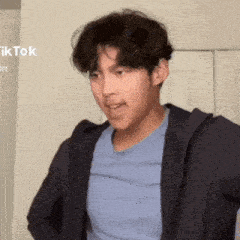 a young man wearing a blue shirt and a black jacket is making a funny face .