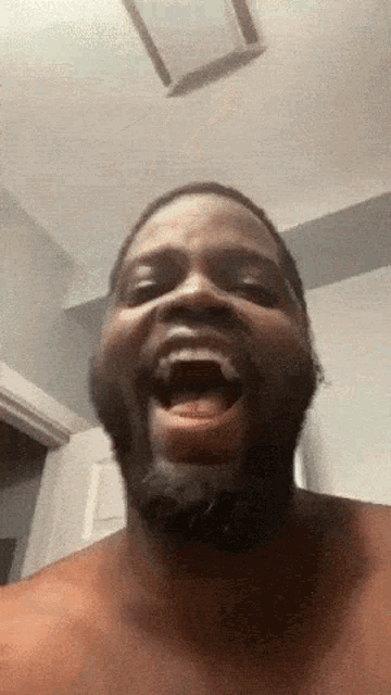 a shirtless man with a beard is smiling with his mouth open