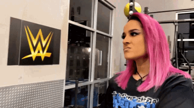 a woman with pink hair is standing in front of a wall with a w on it