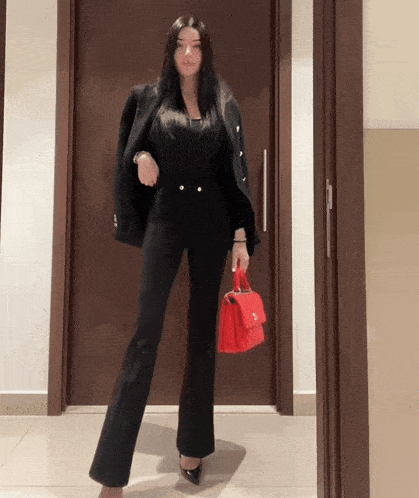 a woman in a black suit is holding a red bag
