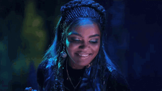 a woman with blue hair and braids is laughing in a dark room