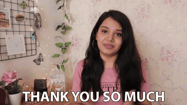 a woman says thank you so much in front of a pink wall