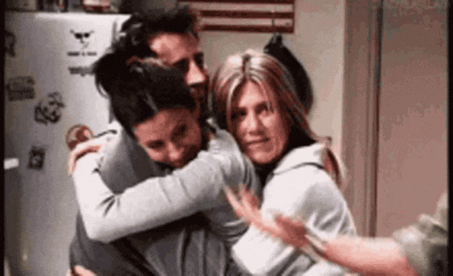 a group of people hugging each other in front of a refrigerator .