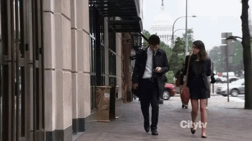 a man and a woman are walking down a sidewalk in front of a building that says citytv on it