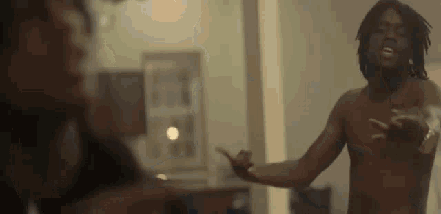 a shirtless man with dreadlocks is standing in a room with a woman .