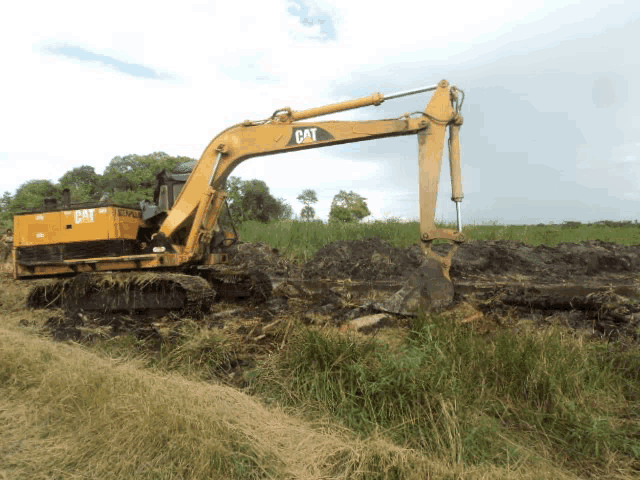 a yellow cat excavator is digging a hole in a field