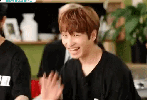 a young man is laughing and waving his hand while sitting in a room with other people .