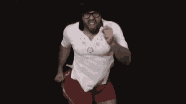 a man wearing a white shirt and red shorts is dancing in the dark .