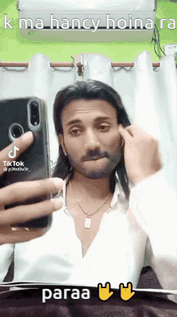 a man with long hair is taking a selfie with a cell phone .