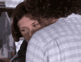 a man and woman are hugging each other and the woman is covering her face .