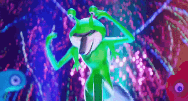 a green frog is dancing on a stage in front of a purple background .