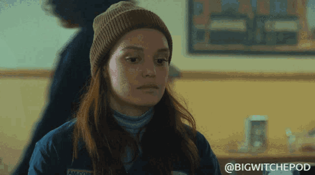 a woman wearing a beanie and a blue jacket with the words bigwitchepod written on the bottom