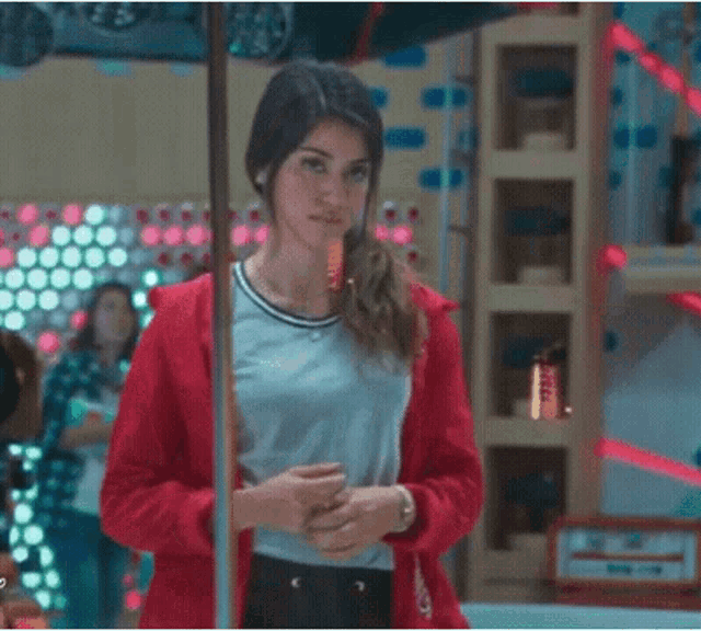 a woman in a red jacket is standing next to a pole in a room .