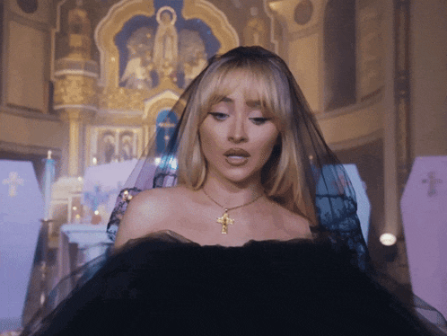 a woman in a black dress with a cross necklace stands in a church