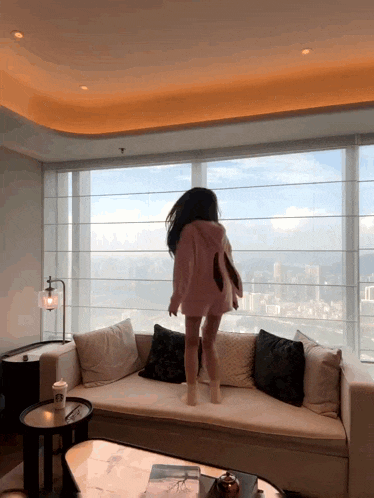 a woman in a pink hoodie is jumping on a couch
