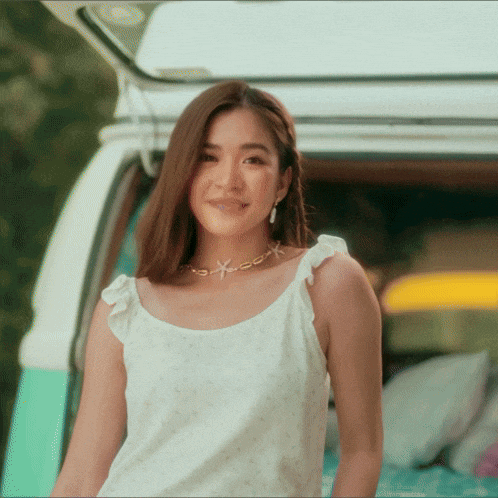 a woman wearing a white top and a necklace with a starfish is standing in front of a van