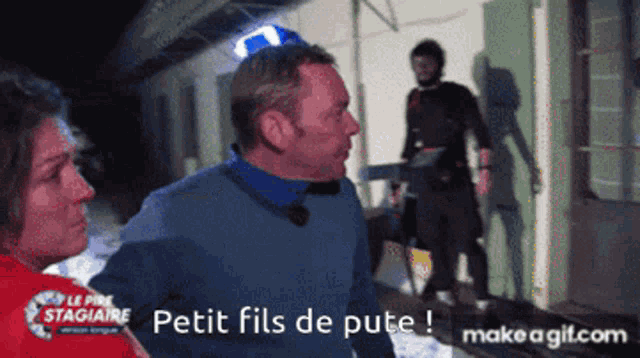 a man in a blue sweater is standing next to a woman in a red shirt with the words petit fils de pute written on it