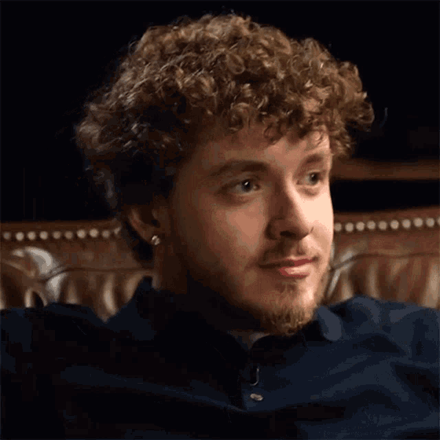 a man with curly hair and a beard is sitting on a leather couch