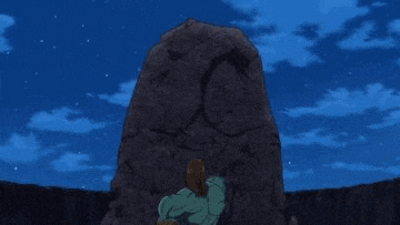 a person is standing in front of a large rock with a face carved into it .