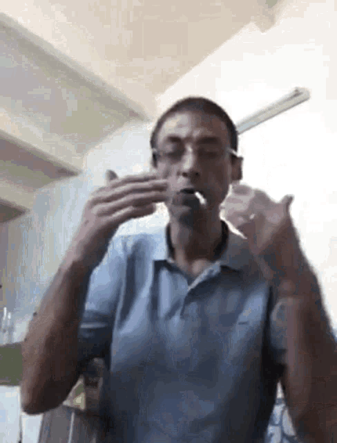 a man in a blue shirt is brushing his teeth with a toothbrush while wearing glasses .