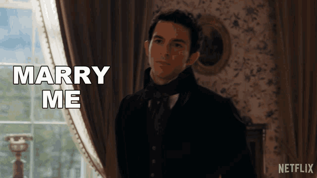 a man in a suit stands in front of a window and says marry me