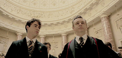 two men in suits and ties stand in a room with columns