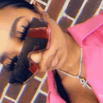 a woman wearing sunglasses and a pink jacket is laying on a brick wall