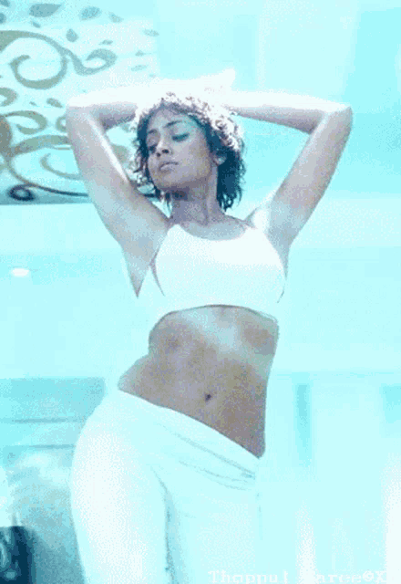a woman in a white crop top and white pants is standing with her hands on her head