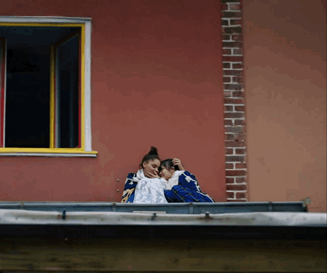 a couple sitting on a balcony with a ladder behind them that says hhh
