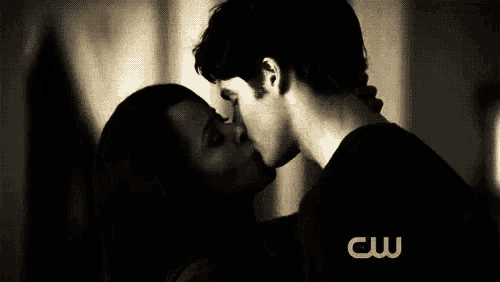 a man and a woman are kissing in a dark room with a cw logo in the background .