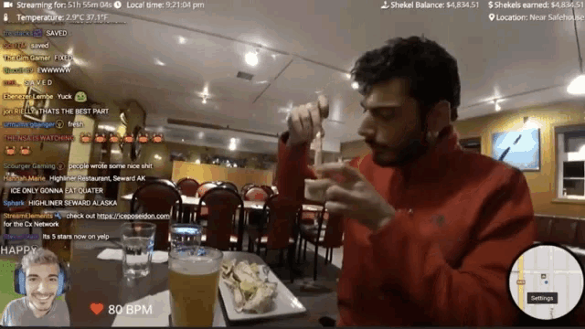 a man in a red jacket sits at a table in front of a screen that says 80 bpm on it