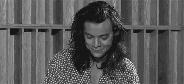 harry styles is smiling in a black and white photo in front of a wooden wall .